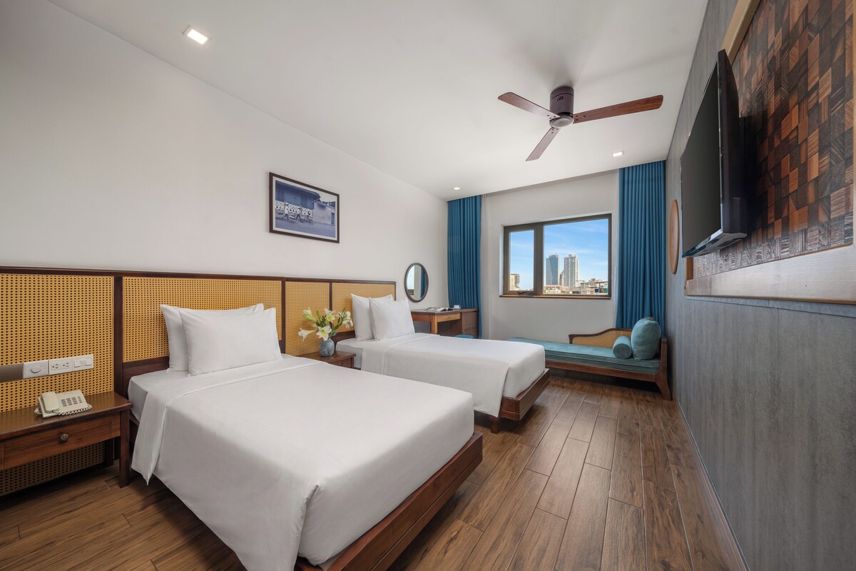 A hotel room with two beds, a desk, a chair, a TV, and a city view.
