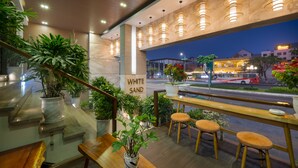 Een restaurant met uitzicht op een straat 's nachts, met een houten bank, potplanten en hangende lampen.