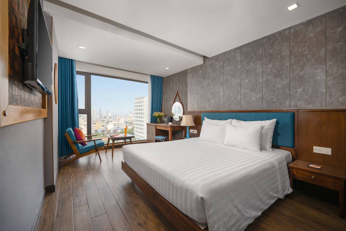 Une chambre d’hôtel avec un grand lit, un bureau avec une chaise, un téléviseur fixé au mur et une vue sur la ville par la fenêtre.