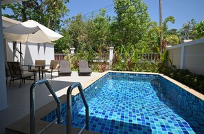A swimming pool with blue mosaic tiles, surrounded by a patio with outdoor furniture and a covered seating area.