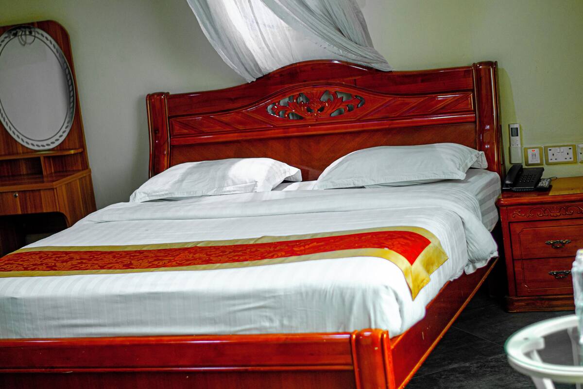 A neatly made bed with a wooden headboard, white linens, and a red and yellow decorative strip.