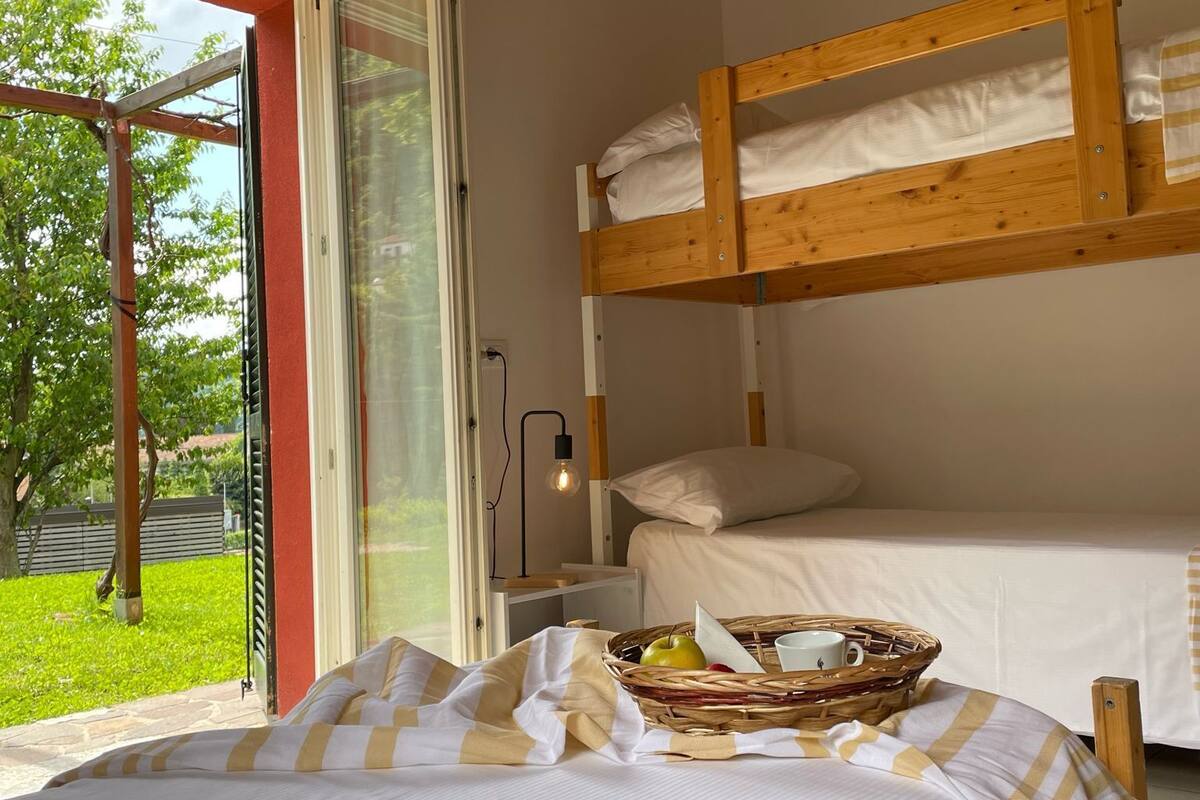 A room with a bunk bed, a window with a view of greenery, and a basket with items on the bed.