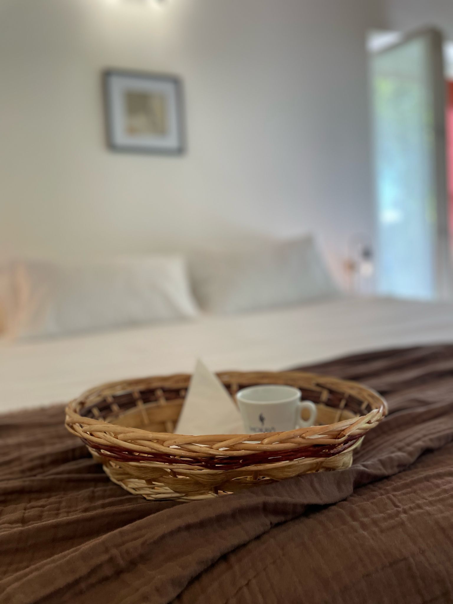 A wicker tray with a white mug and a napkin on a bed with a brown cover.