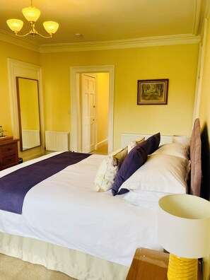 A neatly made bed with a white and purple bedspread, a wooden nightstand with a lamp, and a framed picture on the wall. - West Plean House (Stirling)