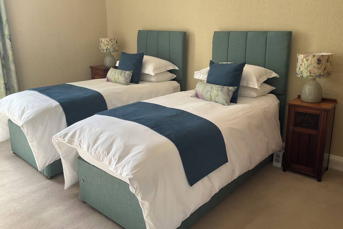 A double bed with a green headboard and white bedding, flanked by nightstands with lamps.