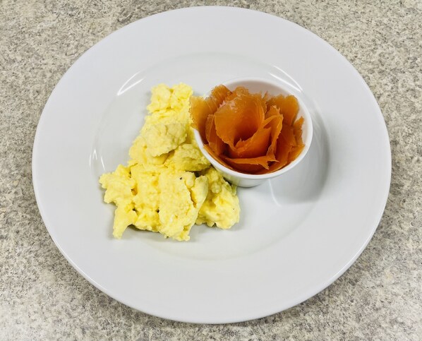 A white plate with scrambled eggs and a bowl of orange slices on a granite countertop. - West Plean House (Stirling)