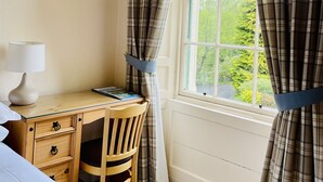 A bedroom with a bed, a desk with a chair, a lamp, and a window with curtains. - West Plean House (Stirling)