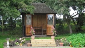 A small wooden structure with a sloped roof, a wooden bench, and potted plants in front. - West Plean House (Stirling)