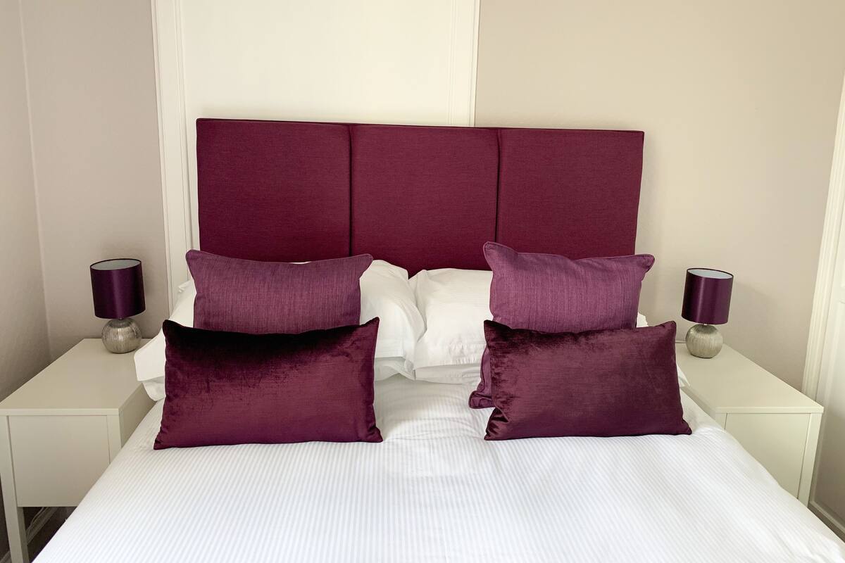 A bed with a white mattress and a maroon upholstered headboard.