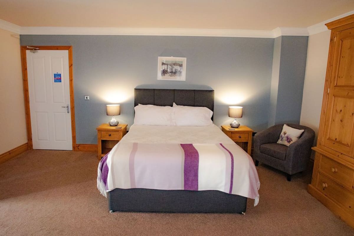 A bedroom with a bed, two bedside tables with lamps, a chair, and a wooden wardrobe.