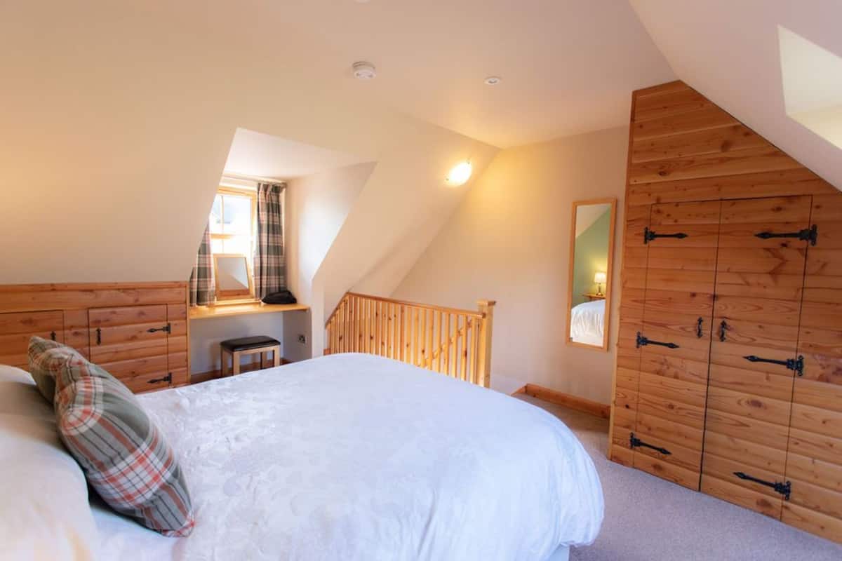 A bedroom with a large bed, a wooden wardrobe, a small desk, and a window with curtains.