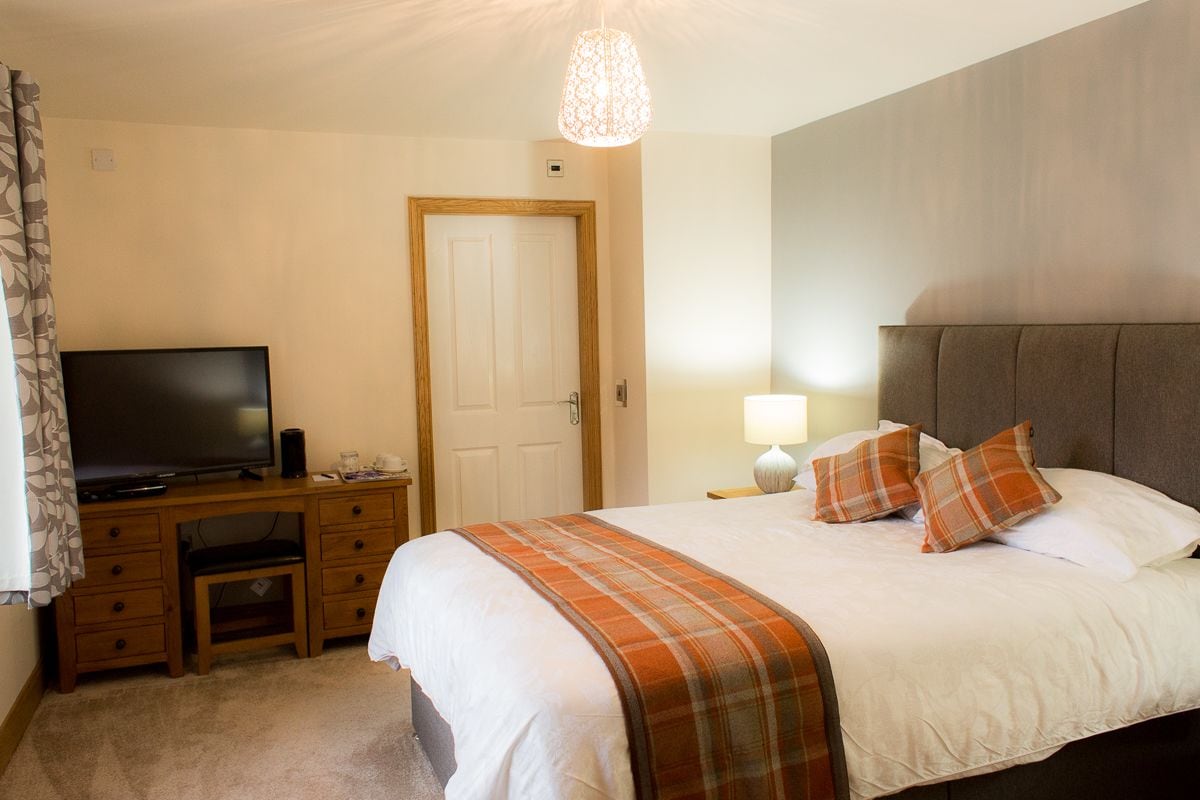 A hotel room with a bed, a television, a desk, and a door.