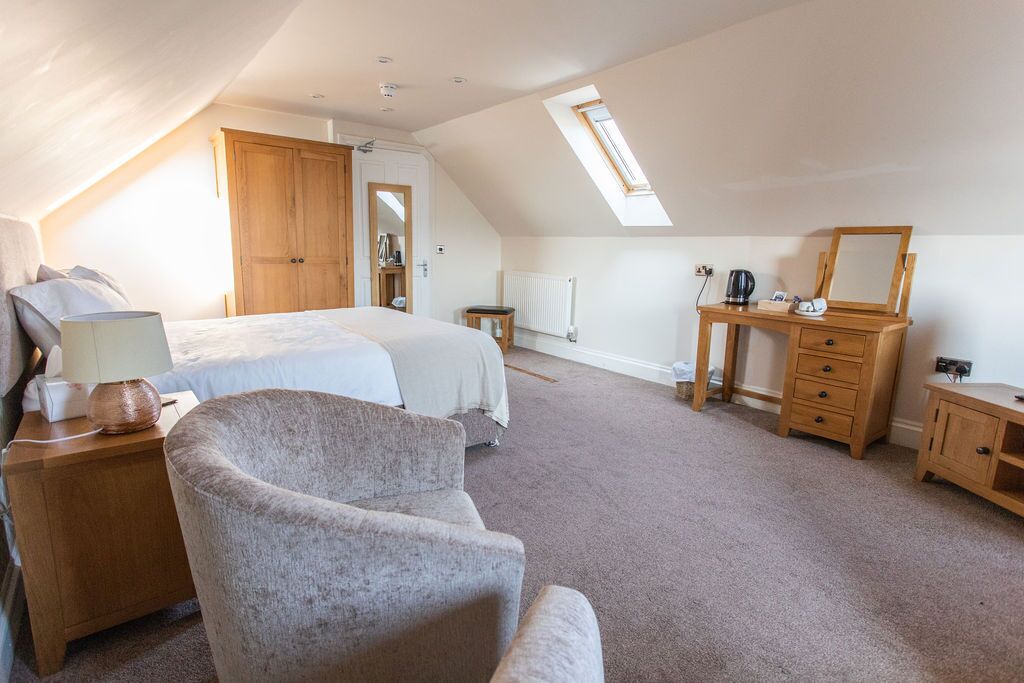 Een slaapkamer met een bed, een bureau, een stoel, een dressoir en een dakraam.