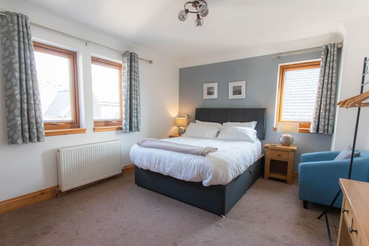 A bedroom with a bed, bedside tables, a chair, and windows.