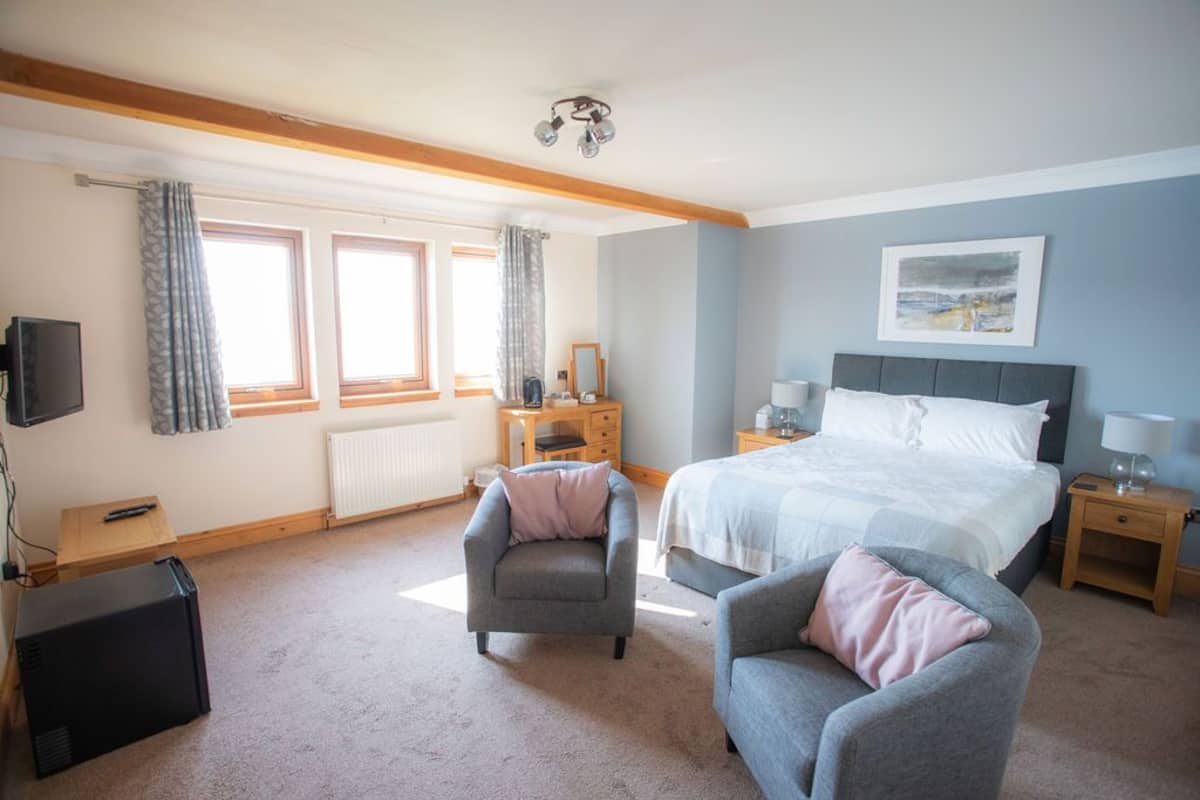 A bedroom with a bed, two armchairs, a dresser, a TV, and a radiator.