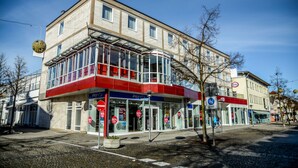 A modern building with large windows, a red and white facade, and a glass entrance. - Hotel Krone (Freilassing)