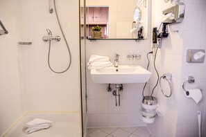 A modern bathroom with a glass shower enclosure, a white sink with a mirror above it, and a towel rack. - Hotel Krone (Freilassing)
