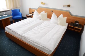 A double bed with white linens, a blue armchair, bedside tables with lamps, and a small desk with a chair. - Hotel Krone (Freilassing)