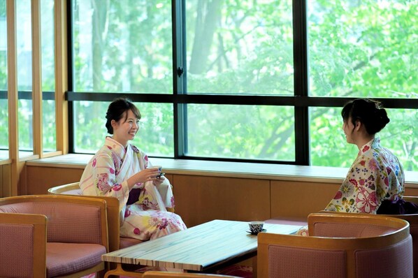 Two individuals in traditional attire seated at a table with a view of greenery through large windows. - Meitoya So (Yamagata)