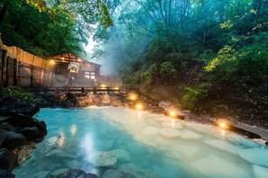 A traditional Japanese onsen with a wooden bathhouse, a stone hot spring, and a forested backdrop. - Meitoya So (Yamagata)