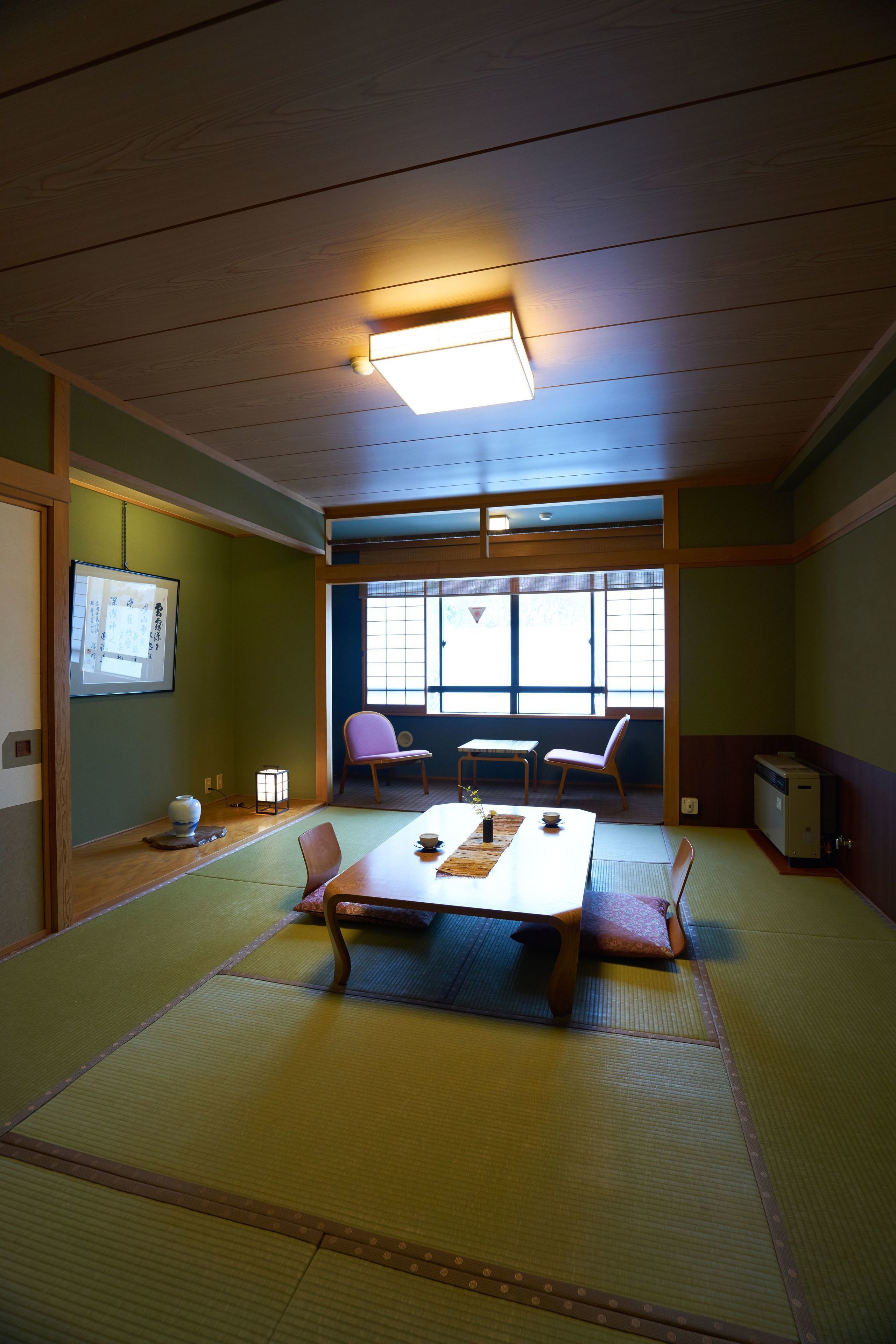 A traditional Japanese room with tatami flooring, a low table with cushions, and a sliding door leading to a window.