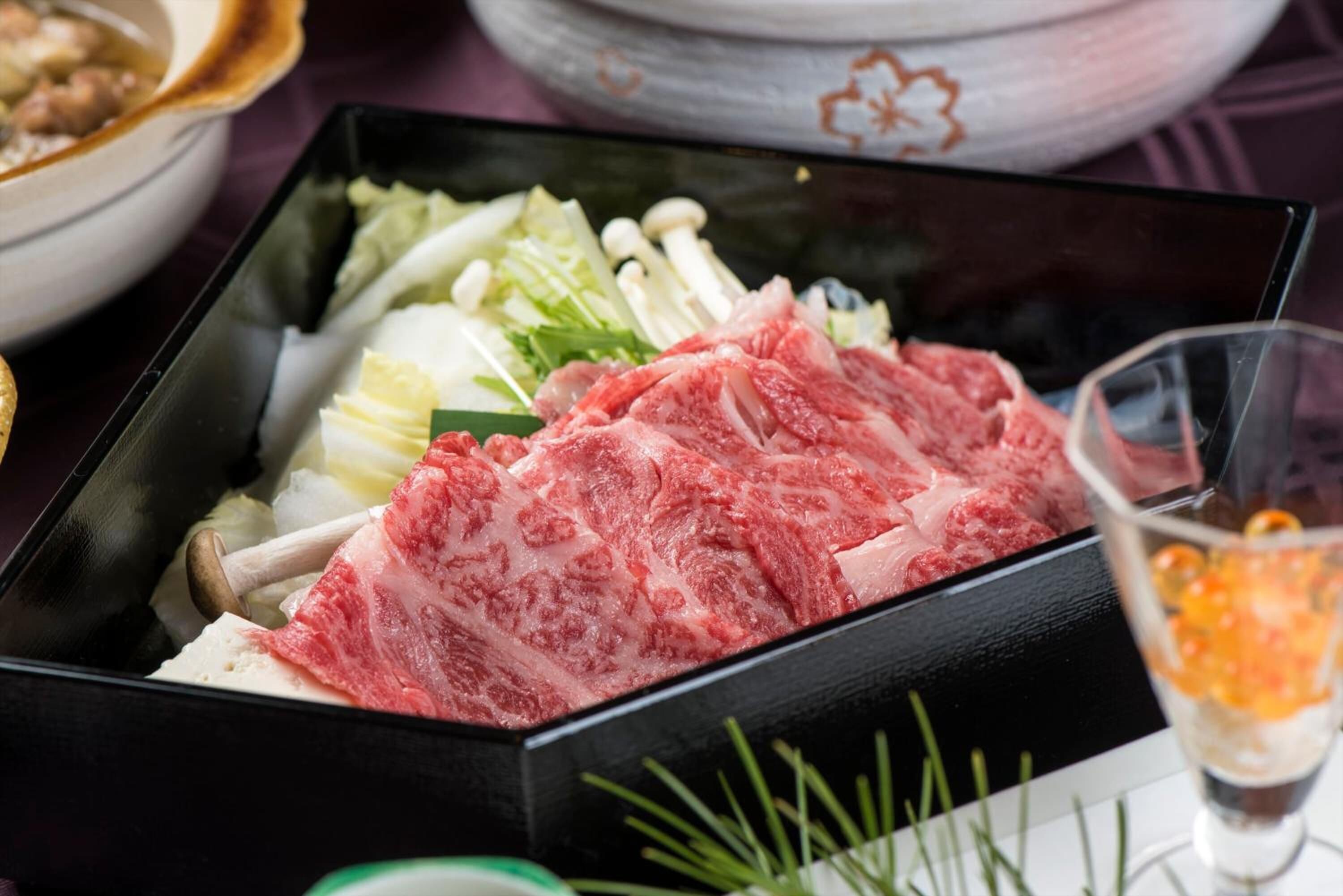 A black tray with raw meat, vegetables, and mushrooms.