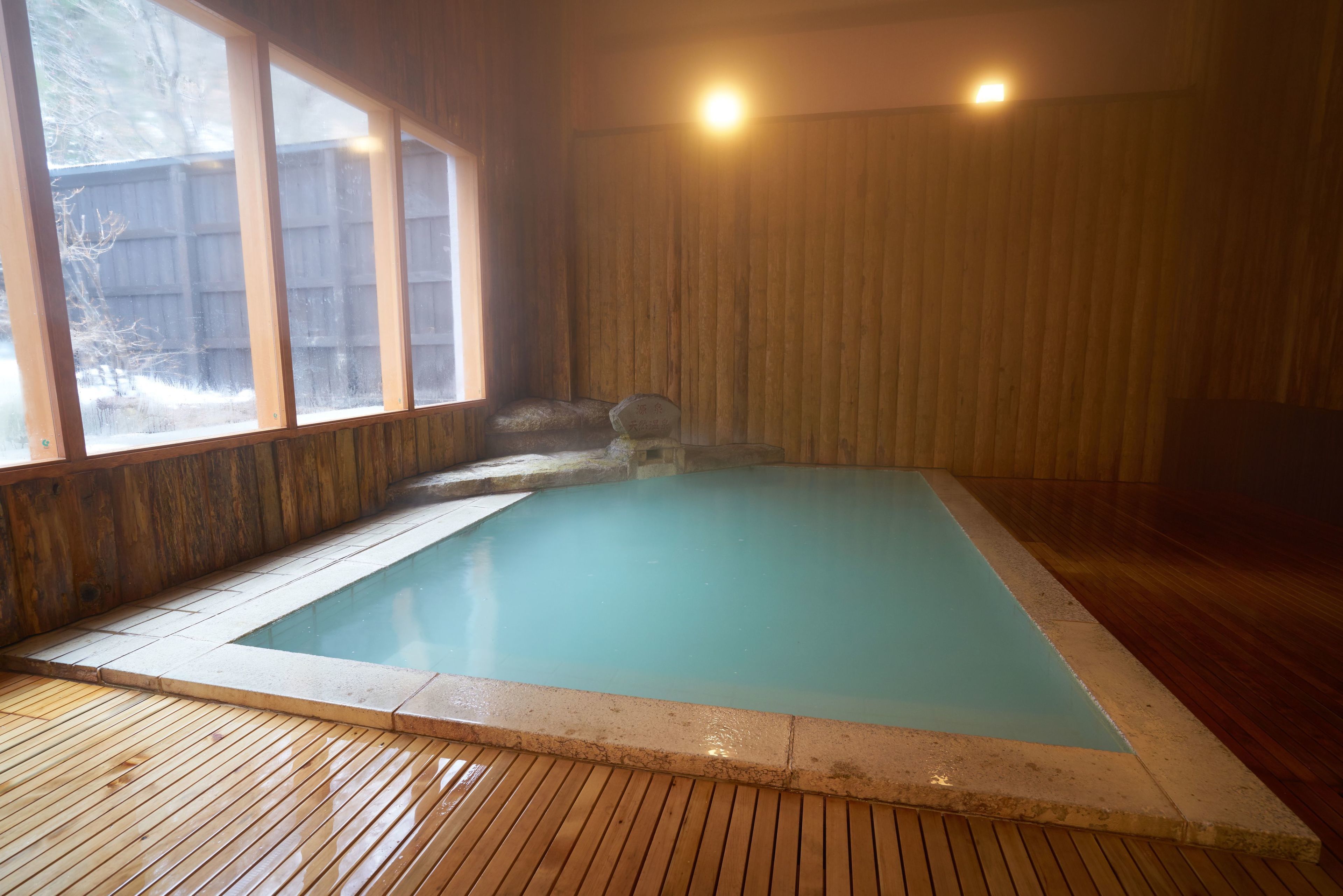 A rectangular indoor swimming pool with a wooden deck surrounding it.