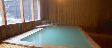 A rectangular indoor swimming pool with a wooden deck surrounding it.