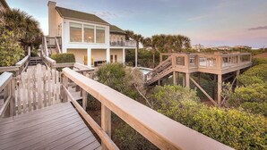 A beachfront property with a wooden deck, a pool, and a two-story house.
