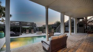 A covered outdoor area with a pool, lounge chairs, and a staircase leading to a deck.