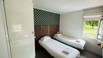 Habitación de hotel con dos camas individuales, cabecera de madera, ventana con vistas a vegetación y una puerta.
