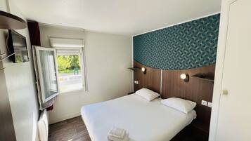 Habitación de hotel con cama, ventana con cortinas, televisión montada en la pared y cabecero de madera con diseño geométrico.