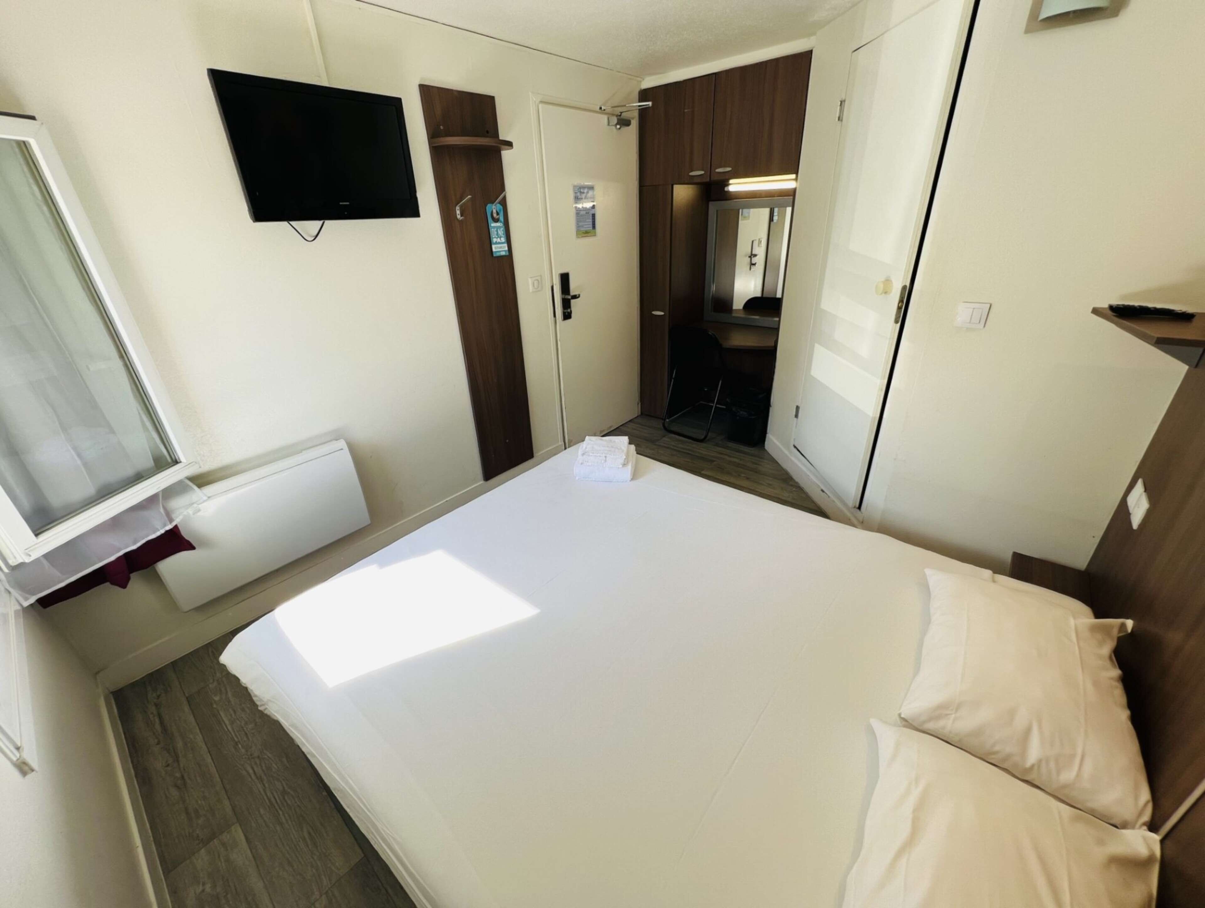 Une chambre d’hôtel avec un lit, un téléviseur fixé au mur, une porte avec un miroir et un petit bureau.
