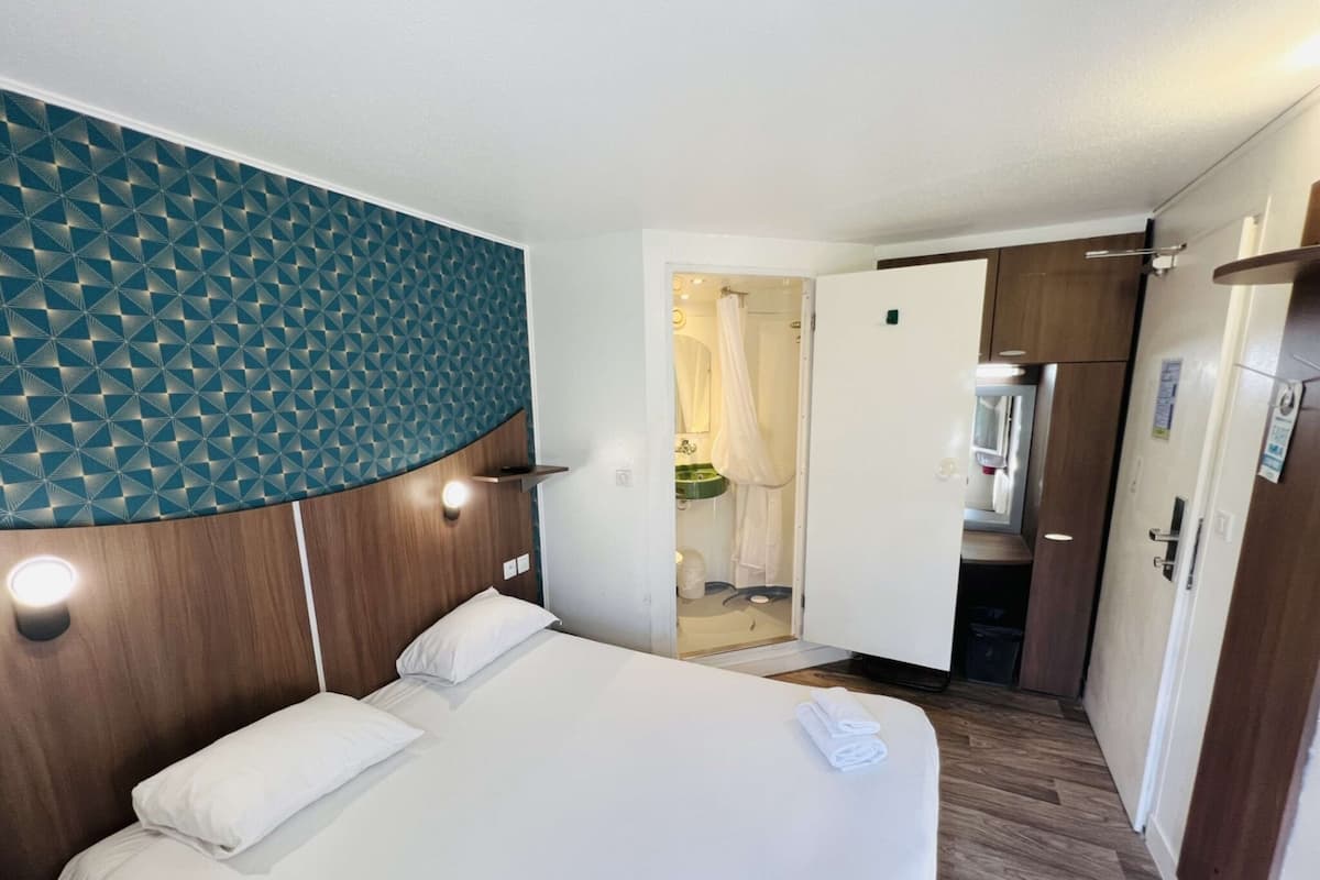 Ein Hotelzimmer mit einem Bett, einem Holzkopfteil, einer Wand mit geometrischem Muster und einem durch eine offene Tür einsehbaren Badezimmer.