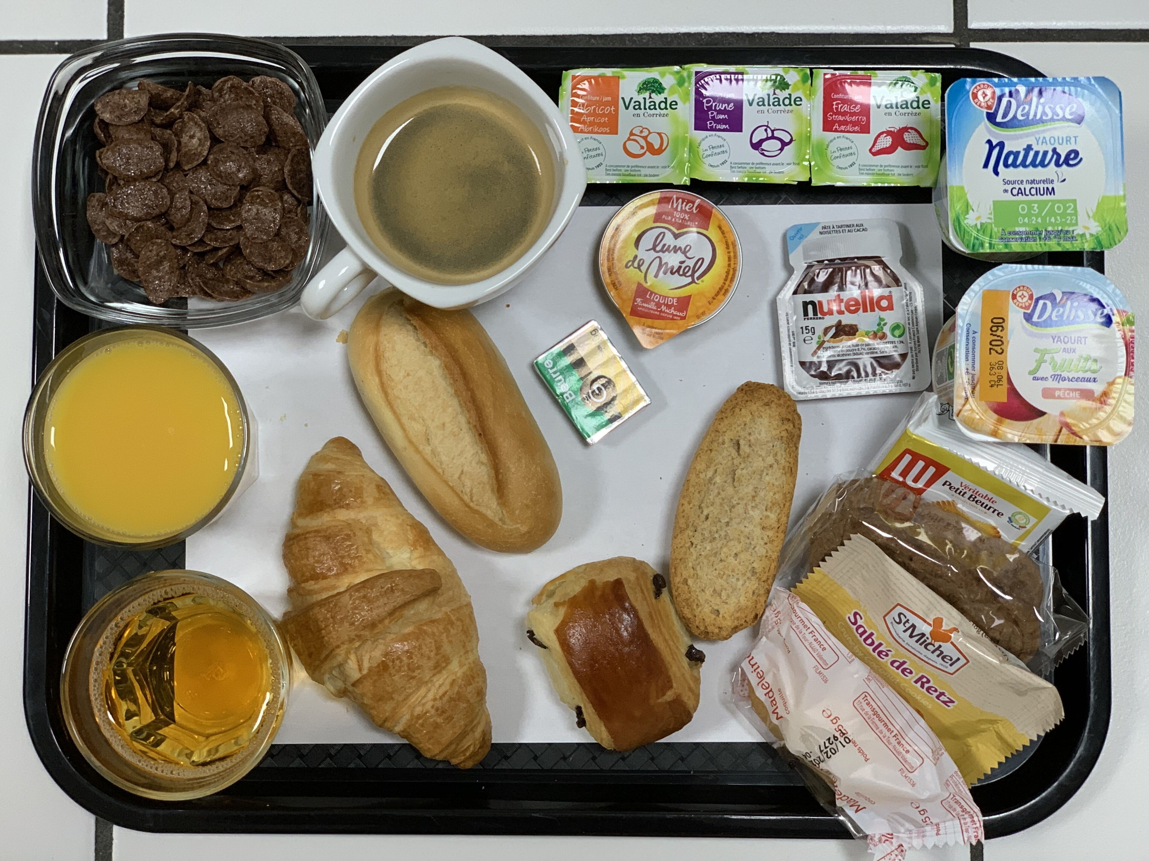 Bandeja de desayuno con diversos alimentos, como cereales, café, jugo, pan, pastelería y productos lácteos.