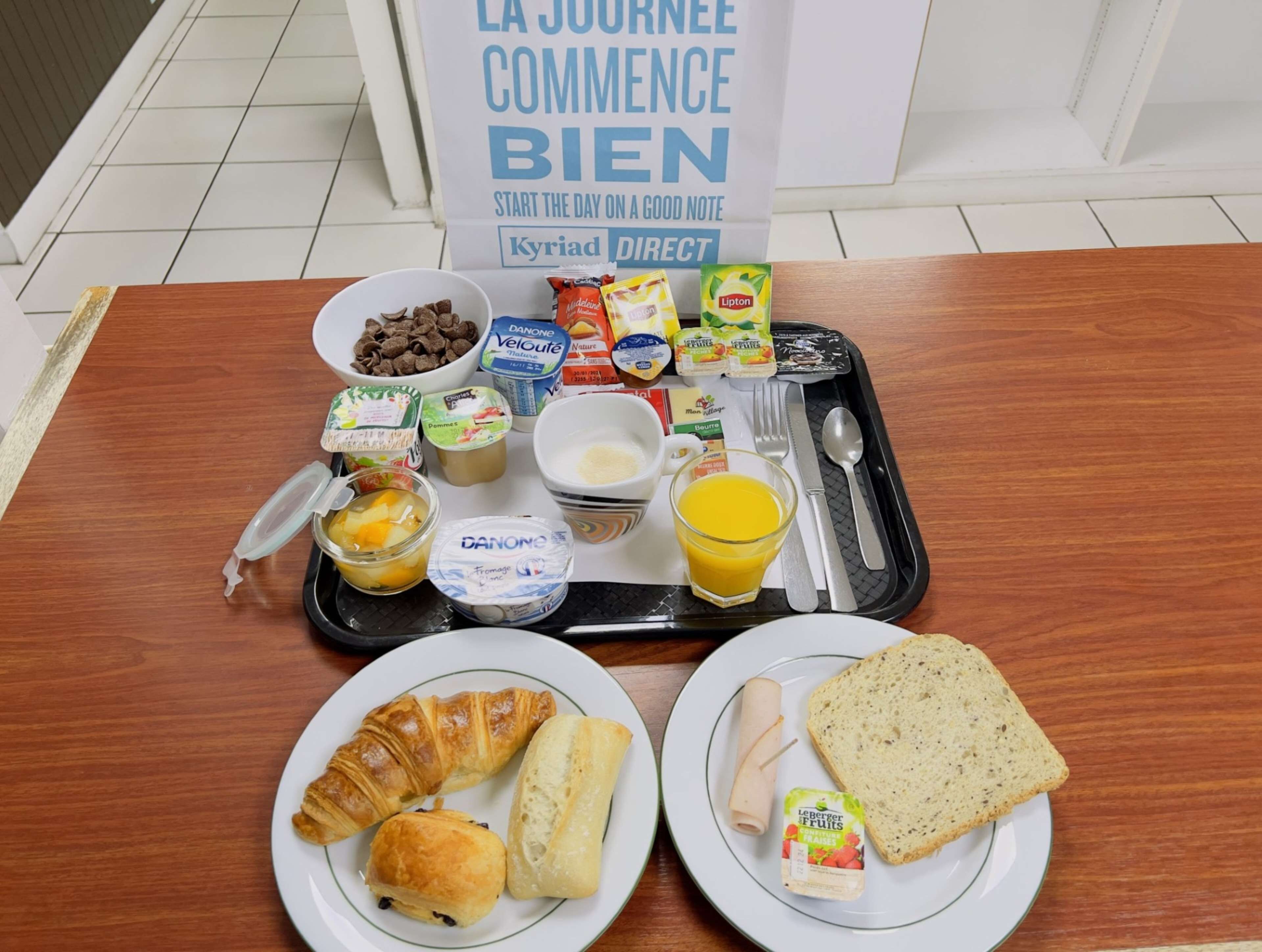 A breakfast tray with various food items including croissants, bread, and a glass of orange juice.