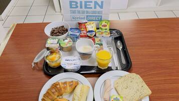 A breakfast tray with various food items including croissants, bread, and a glass of orange juice.