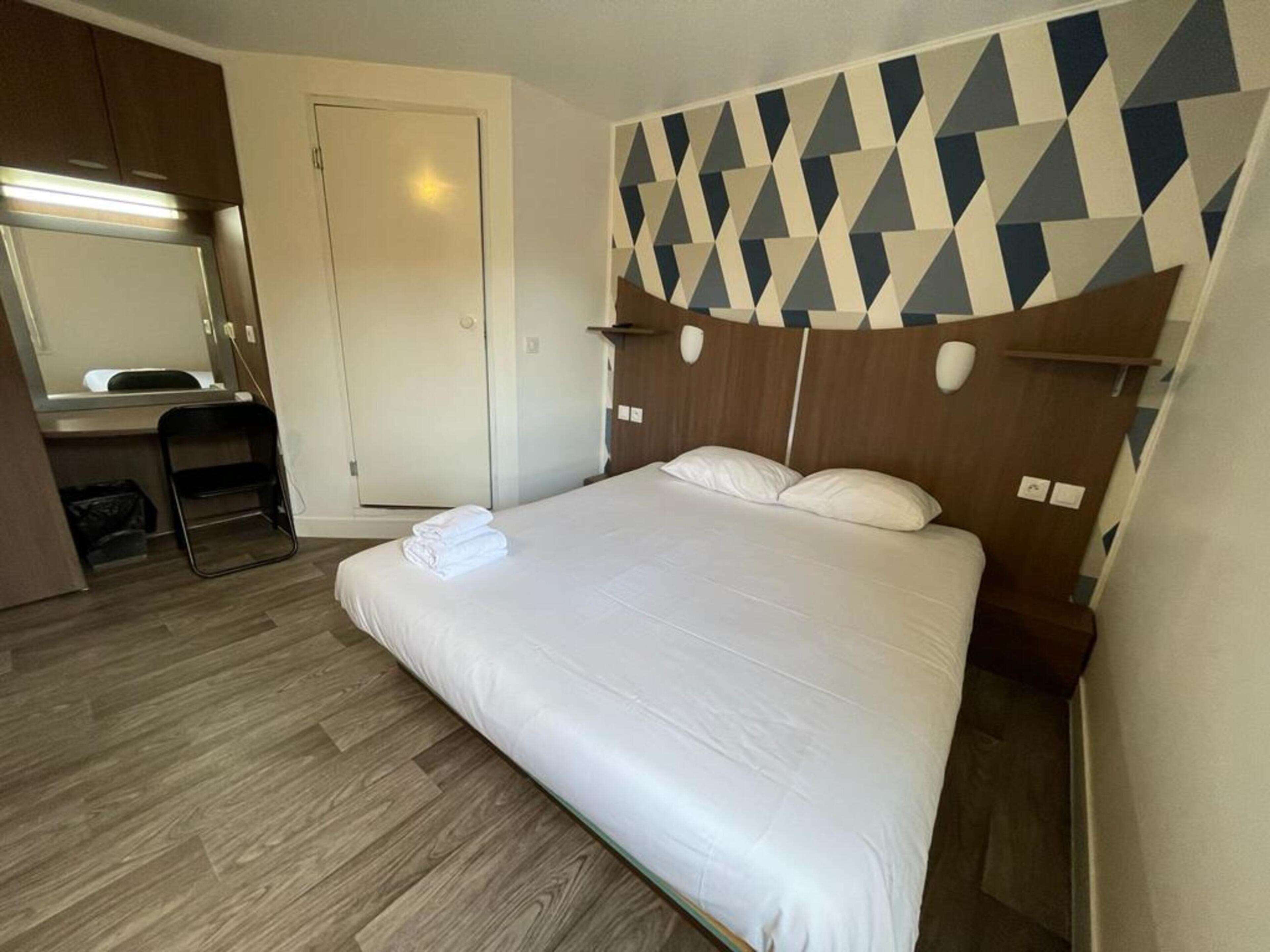 A hotel room with a bed, a desk, a chair, and a mirror.