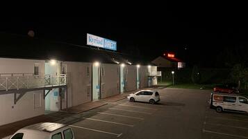 Un estacionamiento con un edificio que dice "Kyriad DIRECT" y un cartel que indica "Best Hotel".