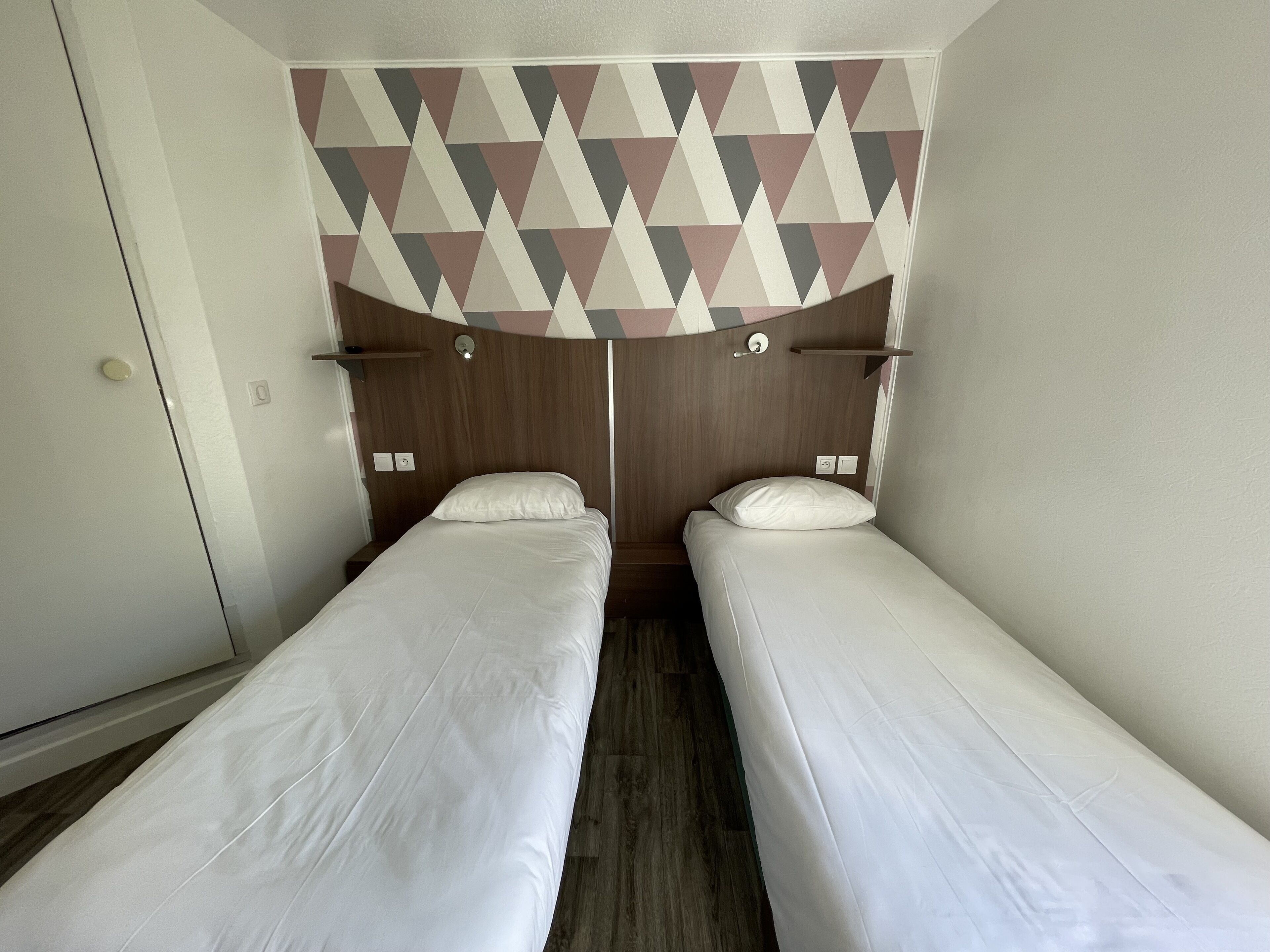 Una habitación con dos camas individuales, cabeceros de madera y un papel tapiz con diseño geométrico.