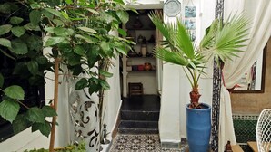 A narrow indoor corridor with a tiled floor, a potted plant, and a staircase leading to an upper level.