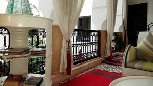 A reading area with a red carpet, books, a lamp, and a view of greenery through a balcony.