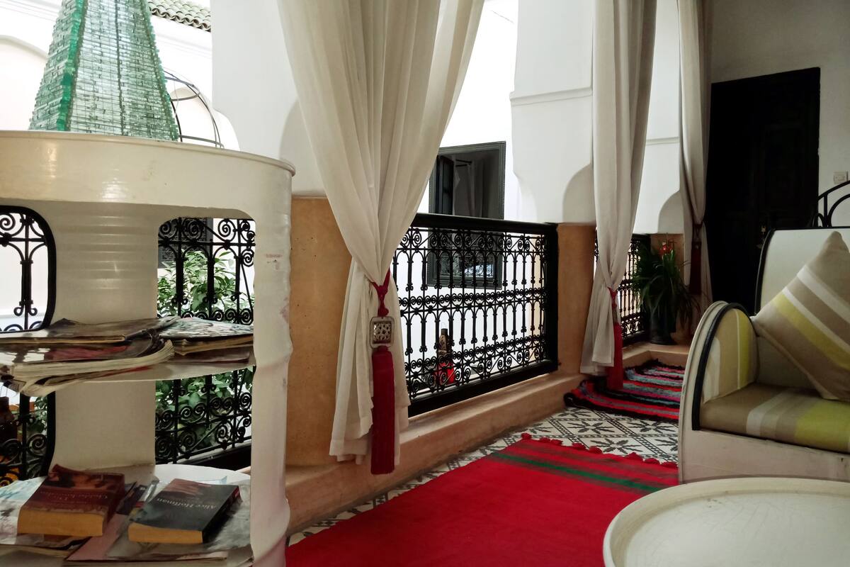 A reading area with a red carpet, books, a lamp, and a view of greenery through a balcony.