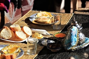 Una mesa con pan, un plato con un sándwich, un vaso de agua y un objeto decorativo azul.
