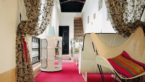 A narrow hallway with a red carpet leading to a white sofa with a colorful cushion. A white table with a blue vase is in the center.