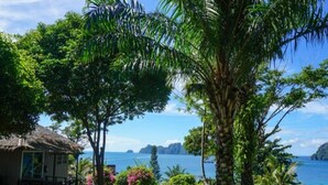 A tropical resort with a thatched-roof hut, a large palm tree, and a view of the sea.