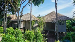 A bungalow-style accommodation with thatched roofs, surrounded by lush greenery and trees.