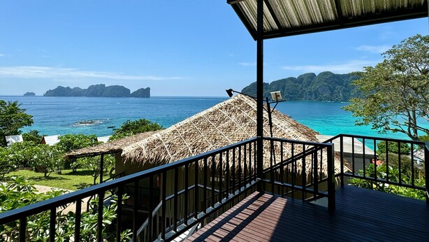A wooden deck with a thatched roof overlooking a turquoise sea and green hills.