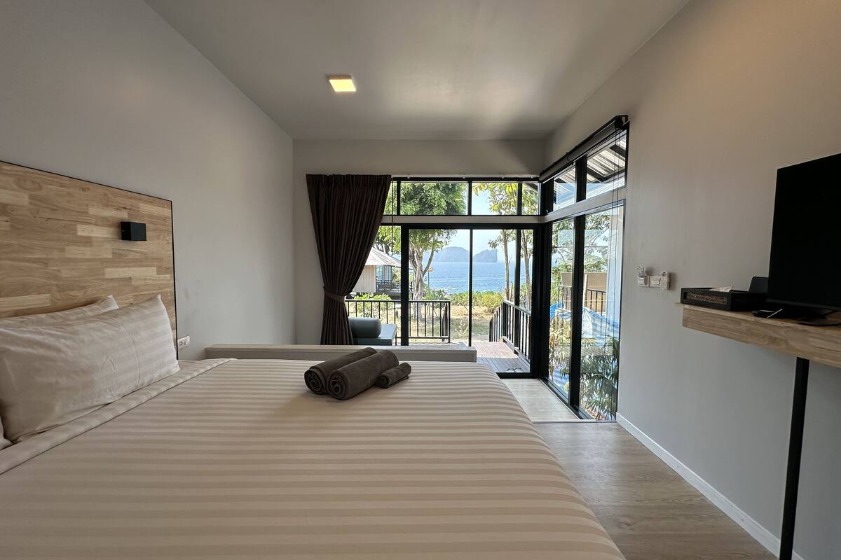 Een moderne hotelkamer met een groot bed, een televisie en een balkon met uitzicht op zee.