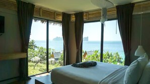 A bedroom with a bed, a ceiling fan, and a view of the ocean.